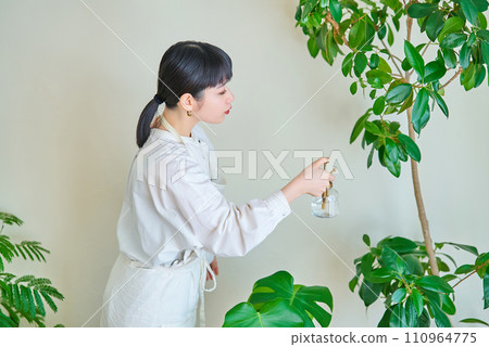 A young woman watering the houseplants in her room A young woman watering the houseplants in her room 110964775