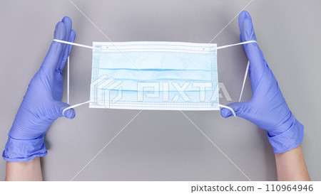 Hand in blue gloves of doctor or nurse holding protective blue face mask over grey background with copy space. New vaccine. Unknown vaccine. Medical gloves. 110964946