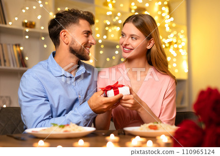 Man presents gift to woman, sharing a joyful moment at dinner 110965124