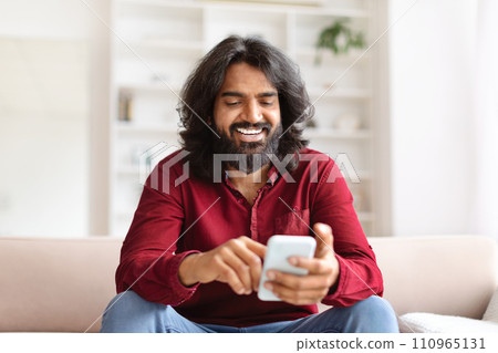 Cheerful bearded man using smartphone at home Cheerful bearded man using smartphone at home 110965131