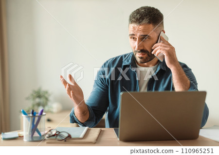 man browses laptop answering unpleasant phone call indoor 110965251