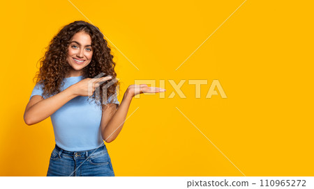 Cheerful woman presenting with hand on yellow, free space 110965272