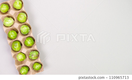 Raw organic Brussel sprouts in brown egg container on grey background, top view. Flat lay, overhead, from above. Copy space. 110965713