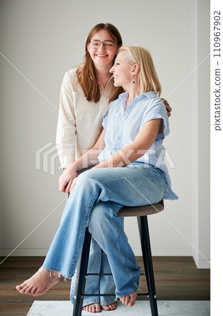 Cute family moment of mom and daughter hugging. Portrait of teenage girl showing her love to mother. Two female in casual clothes smiling and hugging at home. 110967902