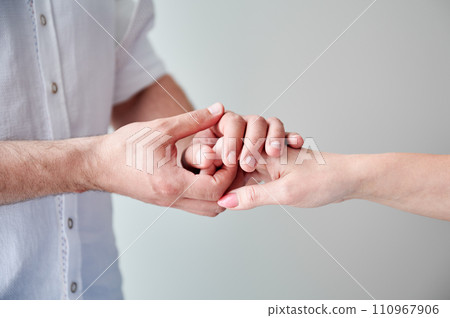 Close up of two hands engaging in delicate touch. Man's and woman's hands on white neutral background. Husband holding hand of his lovely wife. Concept of love, intimacy, support, and trust. 110967906