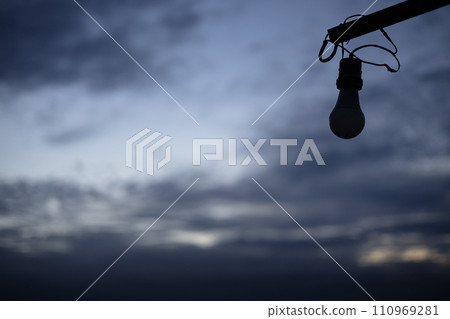 An image of an unlit light bulb against a  cloudy sky. 110969281