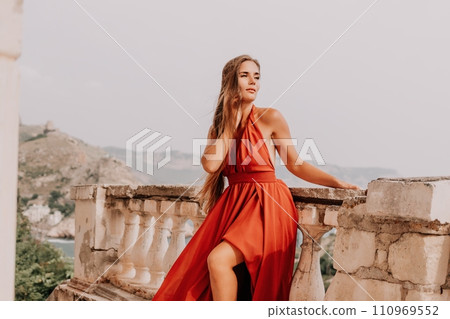 Woman travel portrait. Happy woman with long hair looking at camera and smiling. Close up portrait cute woman in a res long dress posing on backdrop of old travel city near sea Woman travel portrait. Happy woman with long hair looking at camera and smiling. Close up portrait cute woman in a res long dress posing on backdrop of old travel city near sea 110969552