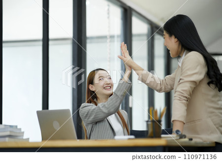 Two women are high-fiving with joy at their success in business. and celebrate performance and teamwork. 110971136