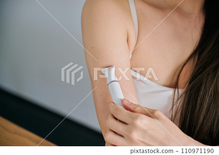 A woman in her 30s shaving her arm hair with an electric shaver 110971190
