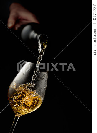 Pouring white wine into a glass. Pouring white wine into a glass. 110973727
