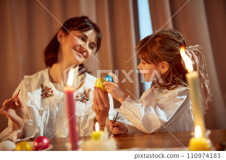 Magic cozy moment. Beautiful mother and her little daughter paining eggs, preparing for Easter holiday at home 110974183