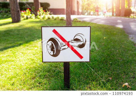 Sign prohibiting the use of hoverboards, placed on a sunny pathway amidst vibrant green grass and trees Sign prohibiting the use of hoverboards, placed on a sunny pathway amidst vibrant green grass and trees 110974193