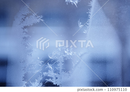 Close up of an abstract blurred frosty patterns on the window, glass with copy space. Blue blurred background. Close up of an abstract blurred frosty patterns on the window, glass with copy space. Blue blurred background. 110975110
