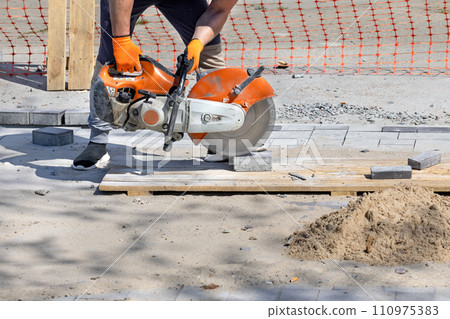 A worker cuts paving blocks at the workplace using a cutting saw and a diamond blade. 110975383