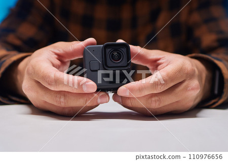 Man holding action camera in hand. It is a compact, lightweight personal camera Man holding action camera in hand. It is a compact, lightweight personal camera 110976656