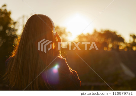 Woman Enjoying Sunset Listening to Music 110979781