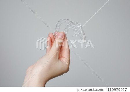 Human hand with transparent invisible dental aligners or braces applicable to orthodontic treatment 110979957
