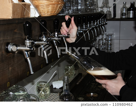 Behind the counter. Women's hands beautifully and easily pour beer into a bottle. Behind the counter. Women's hands beautifully and easily pour beer into a bottle. 110980462