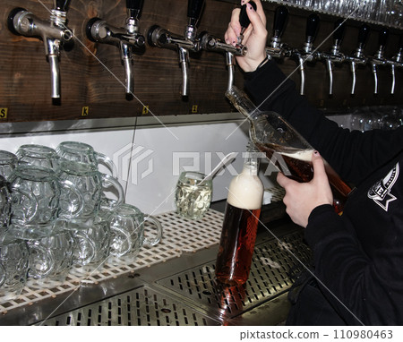 Behind the counter. Women's hands beautifully and easily pour beer into a bottle. 110980463