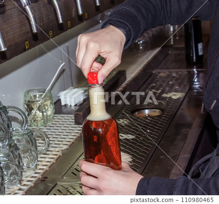 Behind the counter. Women's hands beautifully and easily pour beer into a bottle. Behind the counter. Women's hands beautifully and easily pour beer into a bottle. 110980465