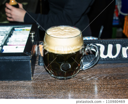 A mug of dark beer foaming on a wooden table. A mug of dark beer foaming on a wooden table. 110980469