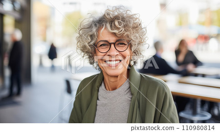 Generative AI The image shows an elderly woman with curly gray hair, wearing glasses and smiling in a cafe setting. Generative AI The image shows an elderly woman with curly gray hair, wearing glasses and smiling in a cafe setting. 110980814