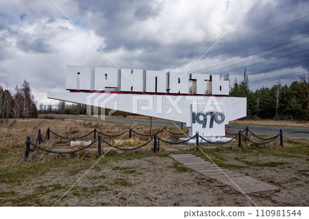 The sign stands under a cloudy sky, with dry grass and bare trees around. Text in cyrillic The sign stands under a cloudy sky, with dry grass and bare trees around. Text in cyrillic 110981544