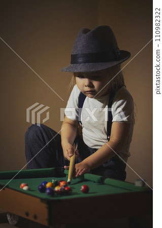 Charming child in retro clothes playing toy billiards Charming child in retro clothes playing toy billiards 110982322