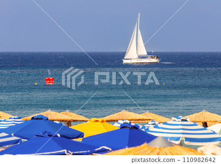 Multi-colored beach umbrellas against the background of a blue sea sky and a yacht. Multi-colored beach umbrellas against the background of a blue sea sky and a yacht. 110982642