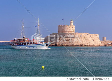 Pleasure tourist boat against the backdrop of the old lighthouse at Fort St. Nicholas in Rhodes. 110982643