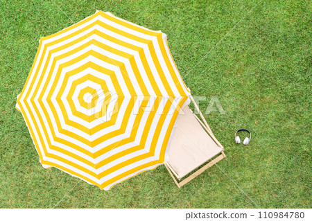 Yellow umbrella with deck chair on the green grass sunbathes at summer day. Top view, drone, aerial view. 110984780