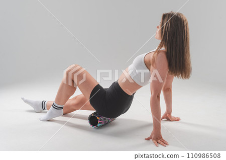 Caucasian woman doing roller exercise for myofascial release on white background. Self-massage of thighs.  110986508