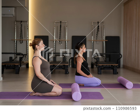 Two pregnant women are sitting on a yoga mat. Prenatal yoga. Two pregnant women are sitting on a yoga mat. Prenatal yoga. 110986593