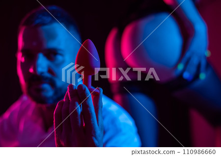 Bearded caucasian man holding an anal plug. Close-up of female buttocks in underwear. Sexual preferences of the couple. 110986660