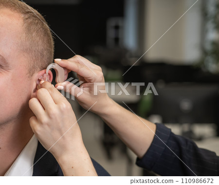Woman putting hearing aid on Caucasian man.  110986672