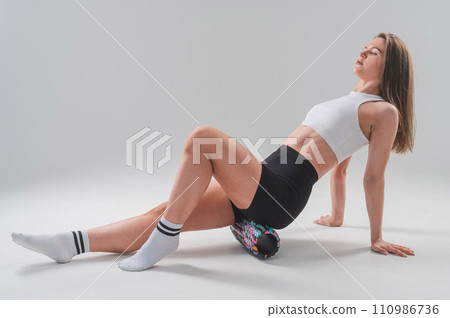 Caucasian woman doing roller exercise for myofascial release on white background. Self-massage of thighs. Caucasian woman doing roller exercise for myofascial release on white background. Self-massage of thighs. 110986736