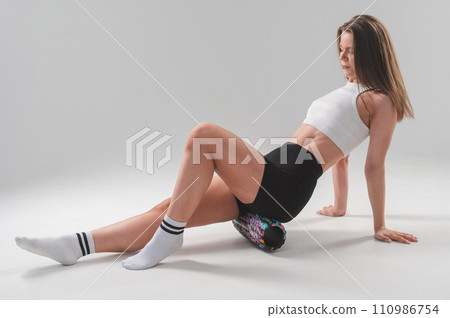 Caucasian woman doing roller exercise for myofascial release on white background. Self-massage of thighs.  110986754