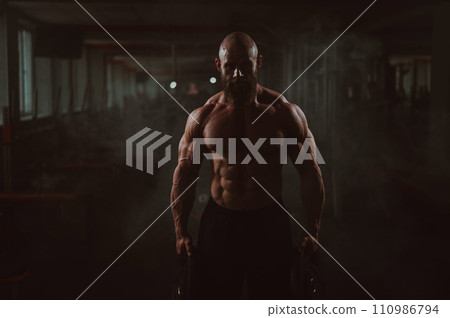 Muscular bald shirtless man holding weight plates. A bodybuilder shows off his form in the gym. 110986794