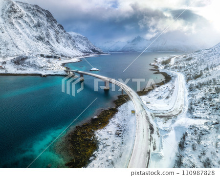 Aerial view of bridge over the sea and snowy mountains in winter Aerial view of bridge over the sea and snowy mountains in winter 110987828