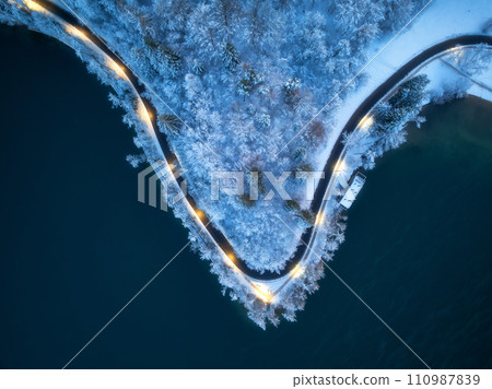 Aerial view of road, snowy forest, lake, street lights at night 110987839