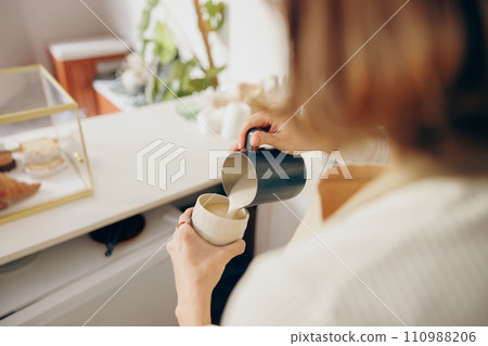 Back view of female barista makes coffee and pours it into a mug while working in coffee shop 110988206