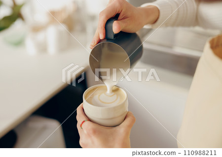 Close up of female barista makes coffee and pours it into a mug while working in coffee shop Close up of female barista makes coffee and pours it into a mug while working in coffee shop 110988211