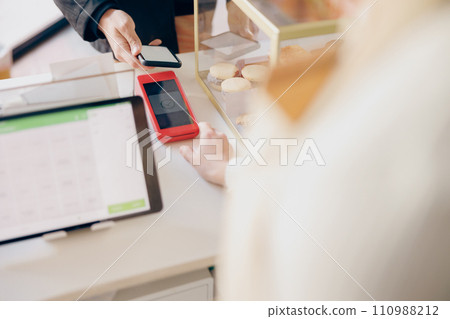 Close up of barista holds out a terminal for contactless paying to a client in coffee shop Close up of barista holds out a terminal for contactless paying to a client in coffee shop 110988212