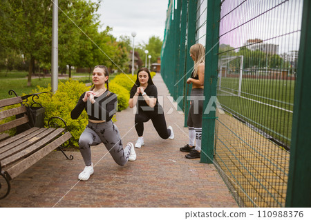 Focused young women do leg exercise at outdoor training Focused young women do leg exercise at outdoor training 110988376