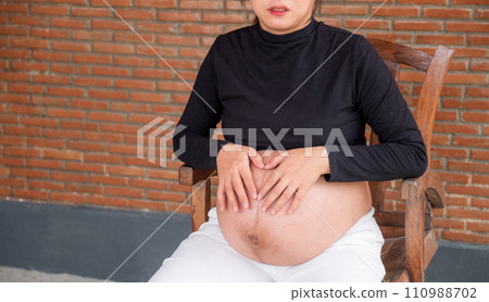 Mom pregnant woman in a dress holds hands on belly on red brick background, Waiting for the birth of your baby with love Mom pregnant woman in a dress holds hands on belly on red brick background, Waiting for the birth of your baby with love 110988702