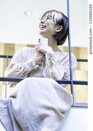 A woman sitting on an indoor bridge and using a smartphone A woman sitting on an indoor bridge and using a smartphone 110989268