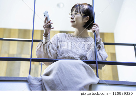 A woman sitting on an indoor bridge and using a smartphone A woman sitting on an indoor bridge and using a smartphone 110989320