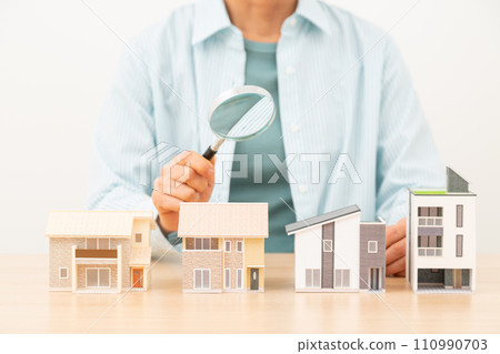 Middle-aged woman with multiple house models and a magnifying glass Middle-aged woman with multiple house models and a magnifying glass 110990703
