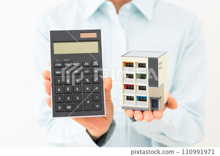 A middle-aged woman smiling while holding an apartment model and a calculator A middle-aged woman smiling while holding an apartment model and a calculator 110991971