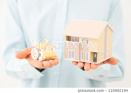 Middle-aged woman with a model of a house and a wheelchair Middle-aged woman with a model of a house and a wheelchair 110992194
